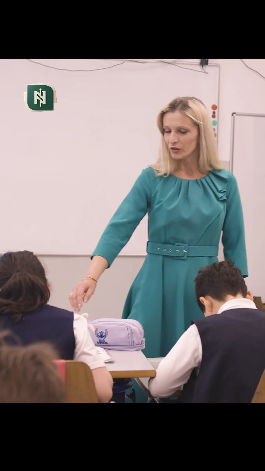 O învățătoare în picioare, în fața elevilor, în clasă.