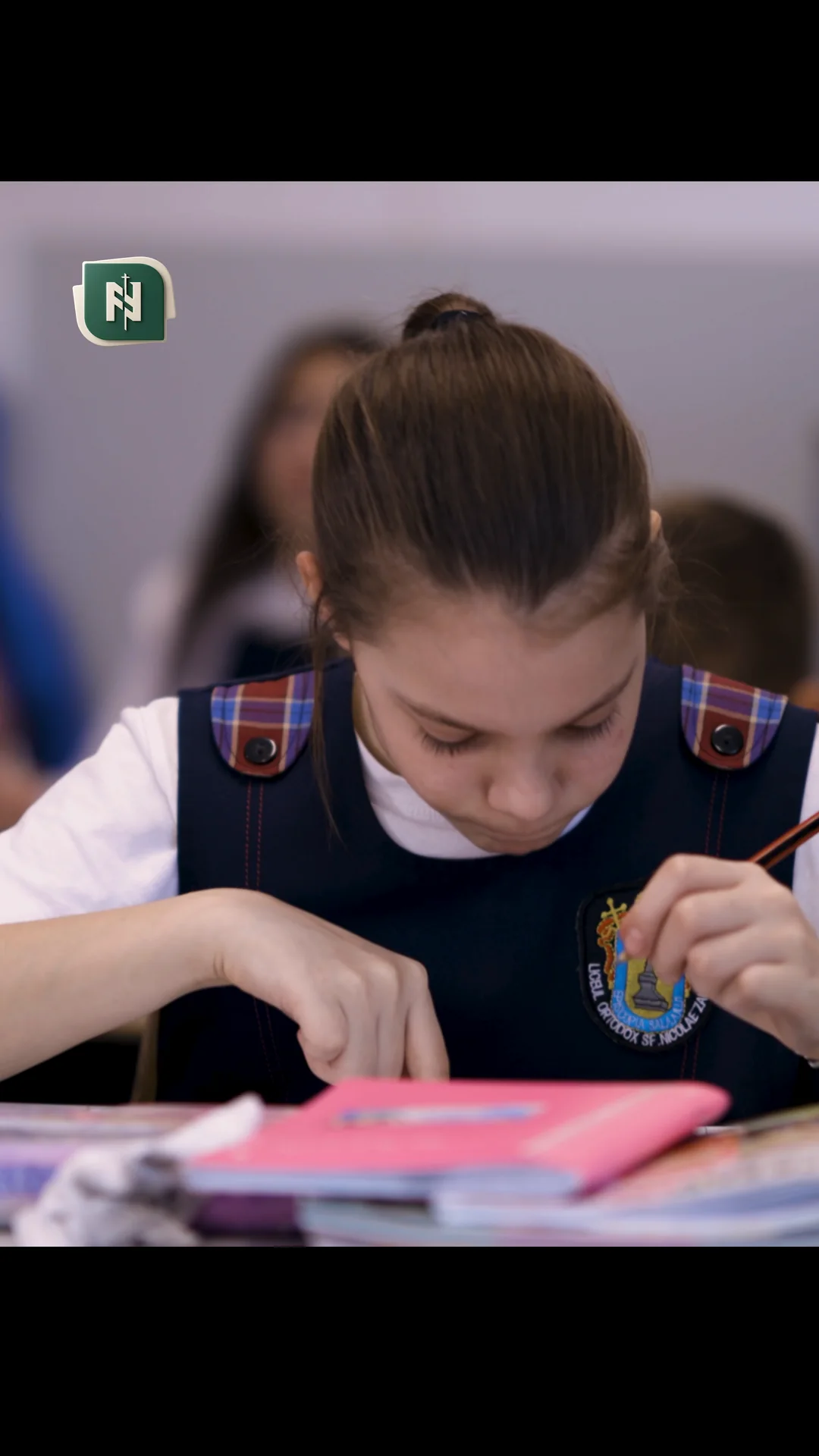 O elevă care scrie în caiet, în bancă.