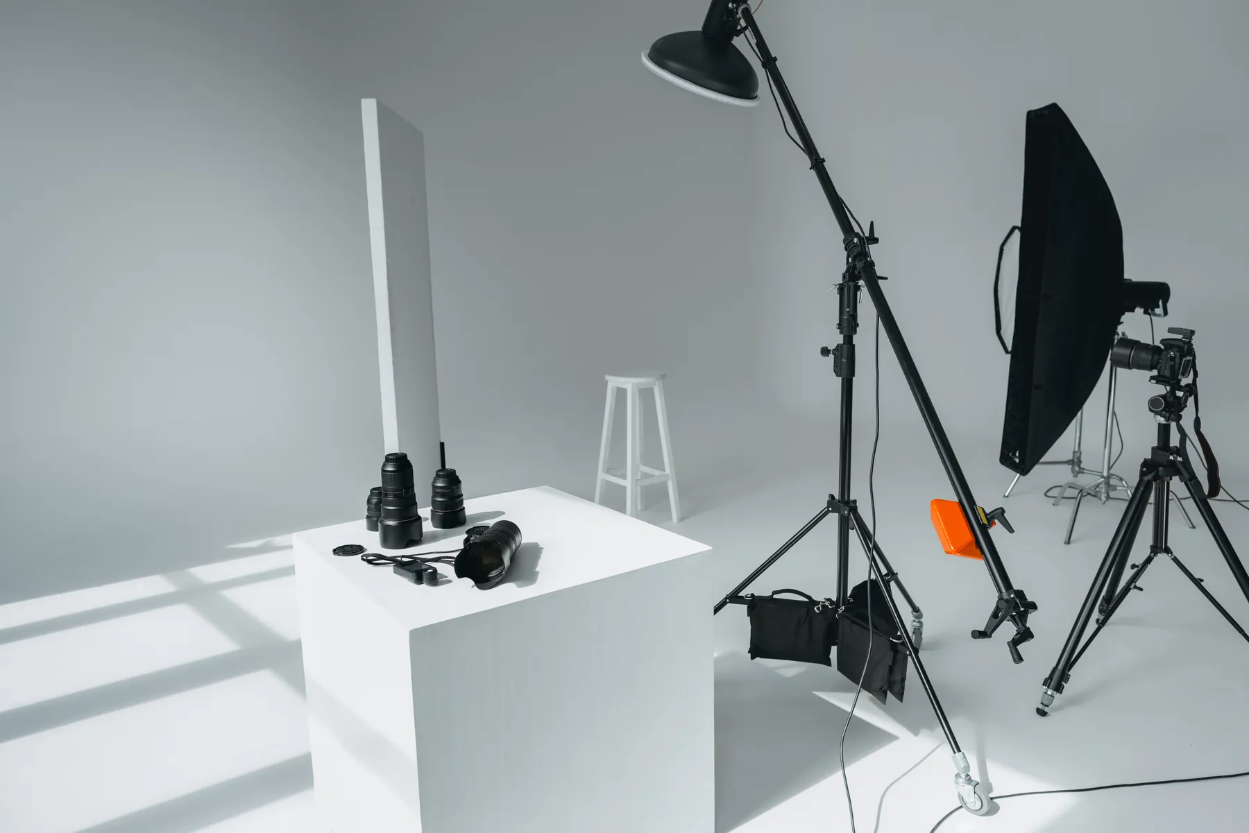 Studio foto cu lumini, softbox, aparate și obiective așezate pe un podium alb.